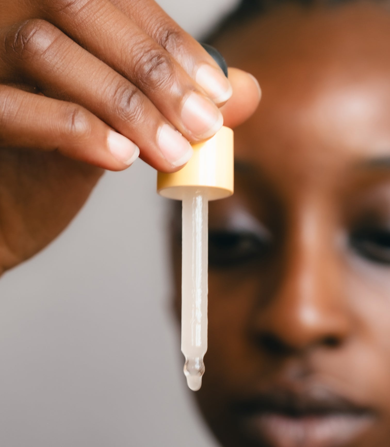 Person holding a dropper close to their face against a neutral background