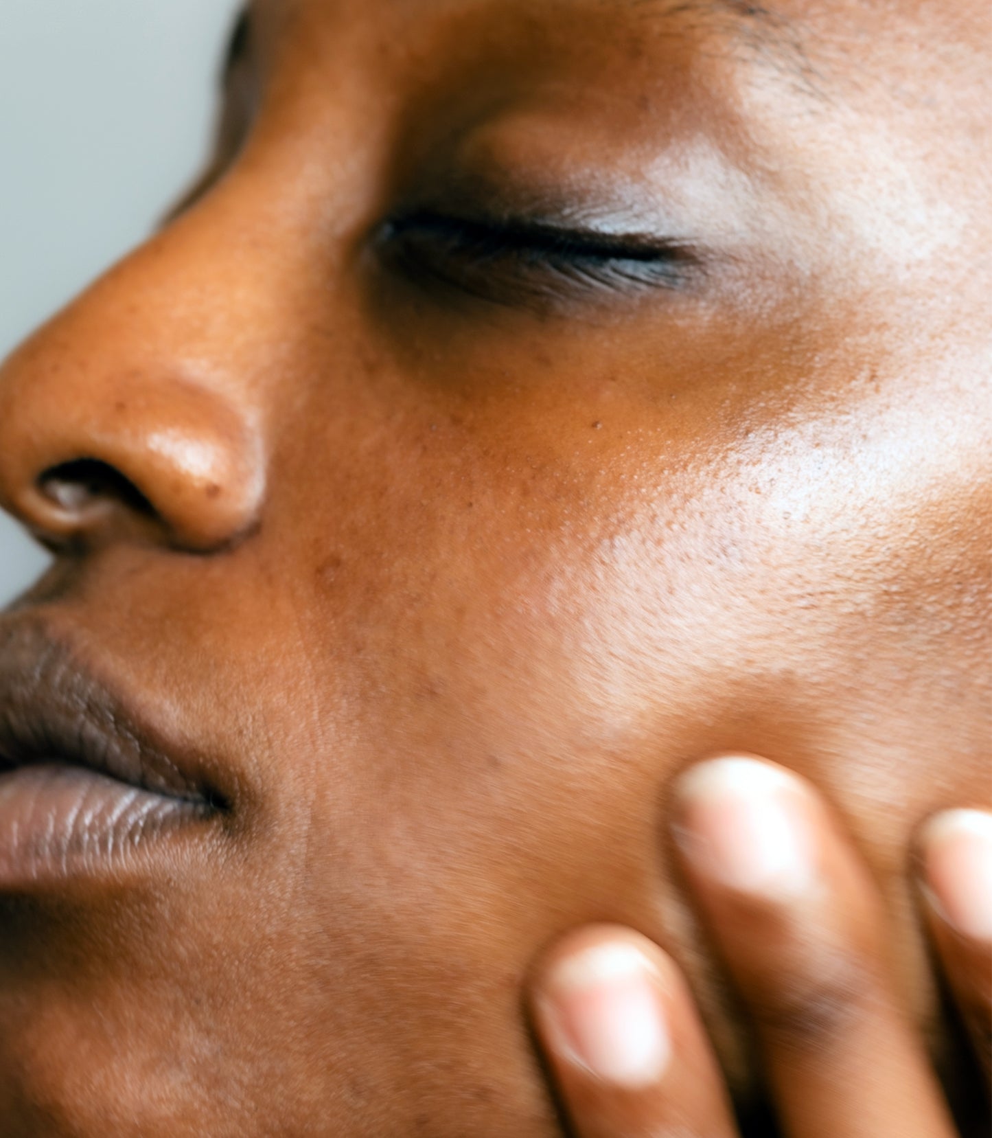 Close-up of a person's face with a hand on their cheek, against a neutral background