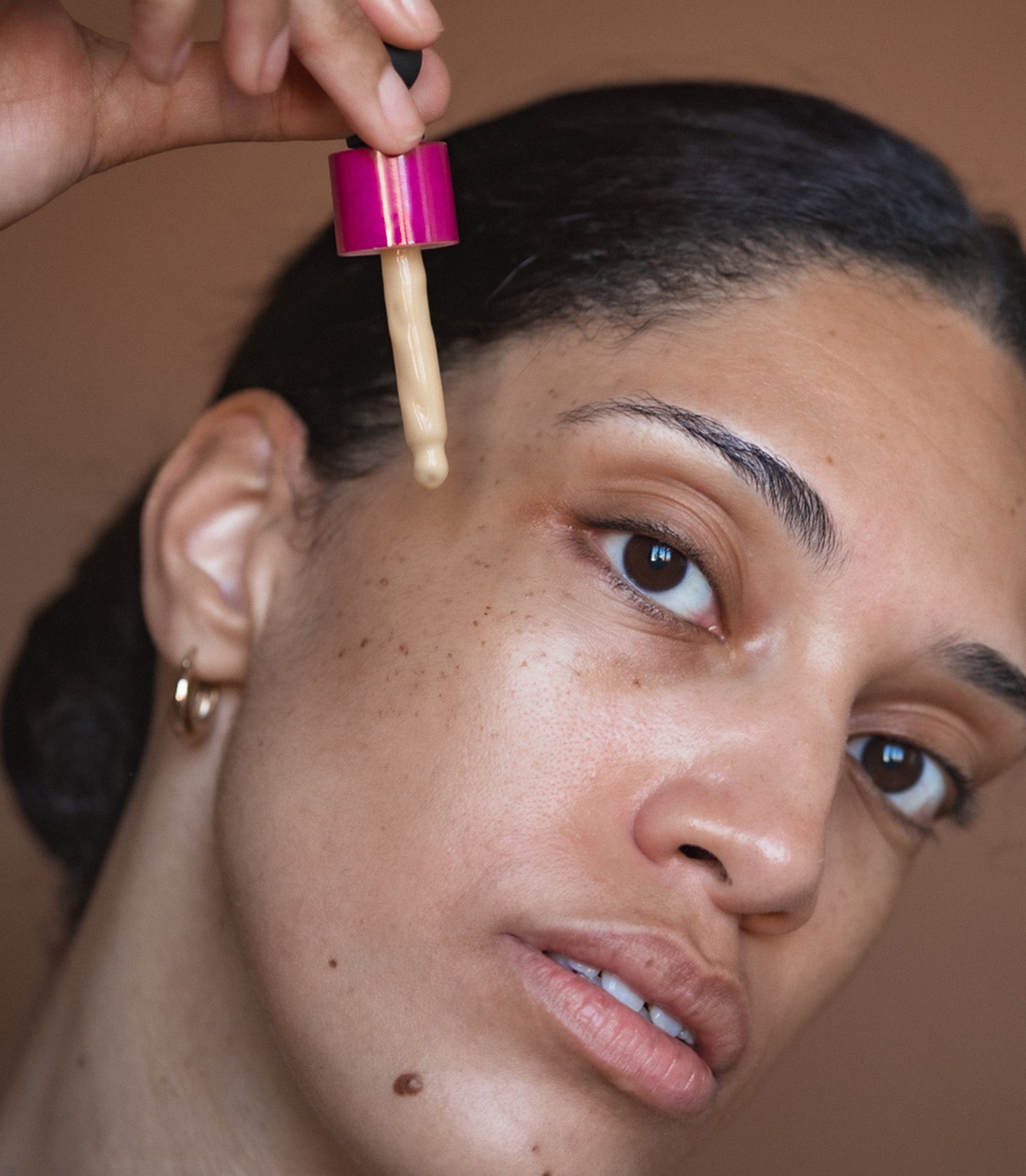 Person applying a dropper of liquid to their face against a neutral background