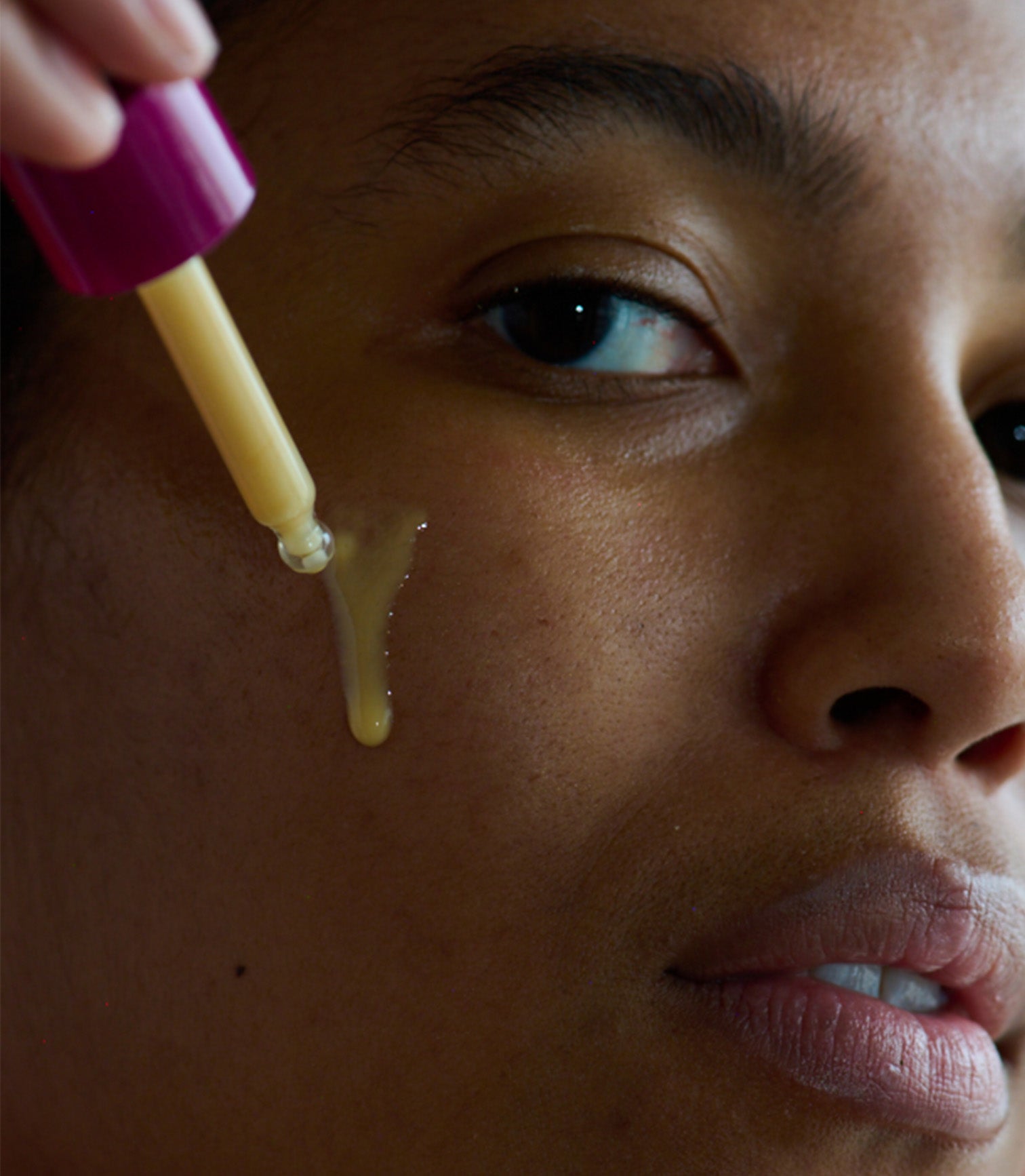 Person applying a yellow substance from a dropper to their face.