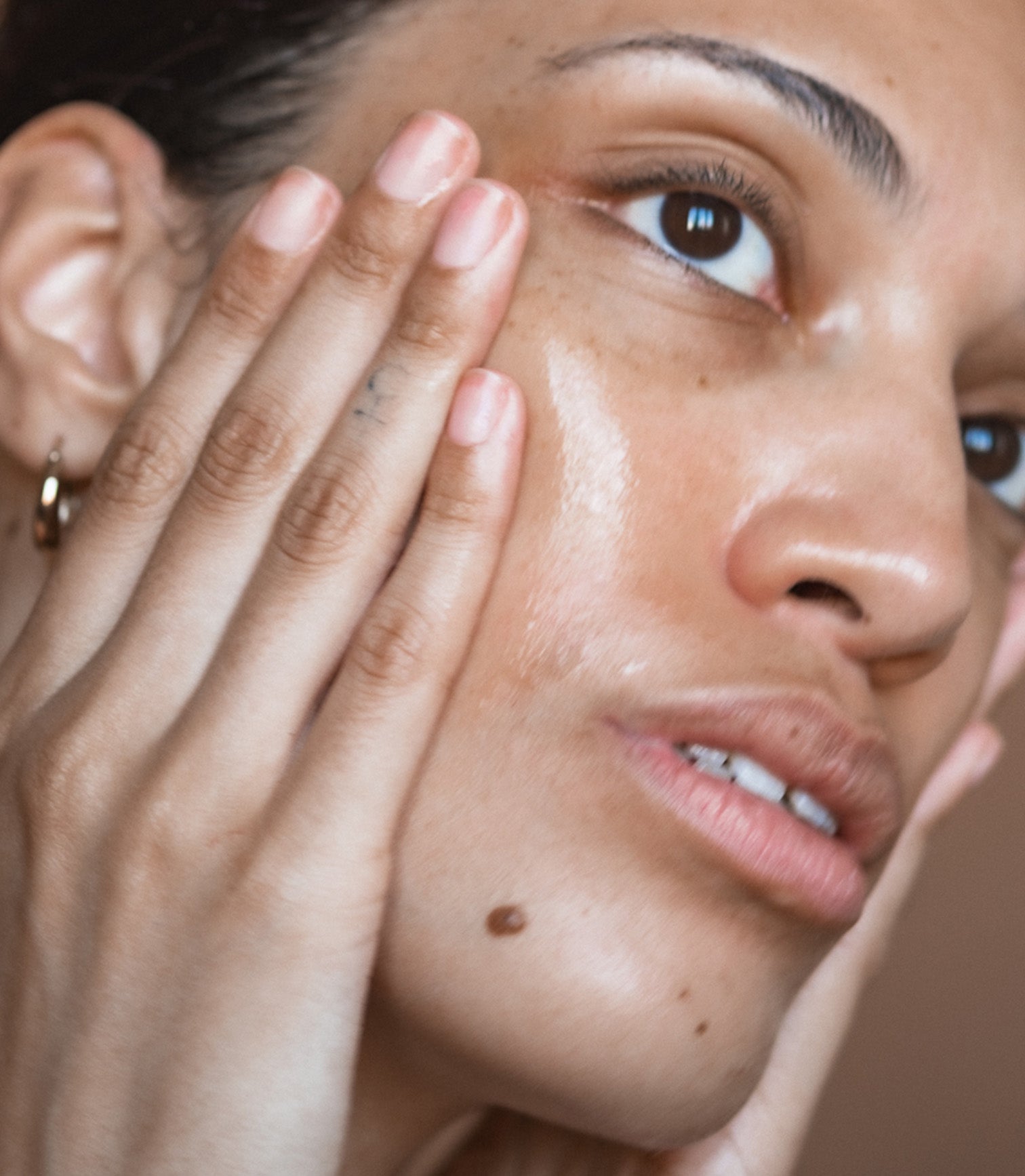 Close-up of a woman's face with one hand covering her eye, showing skin texture and makeup.