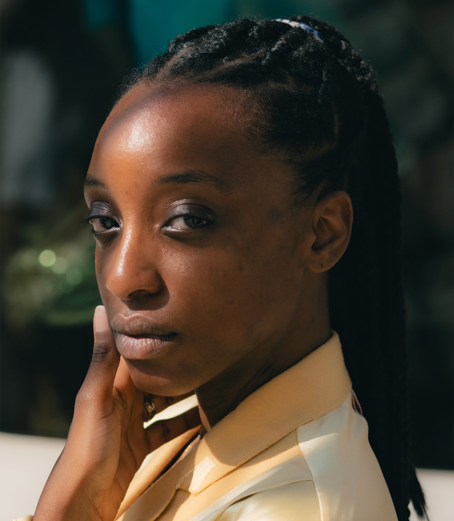 Woman with braided hair wearing a beige shirt against a blurred background