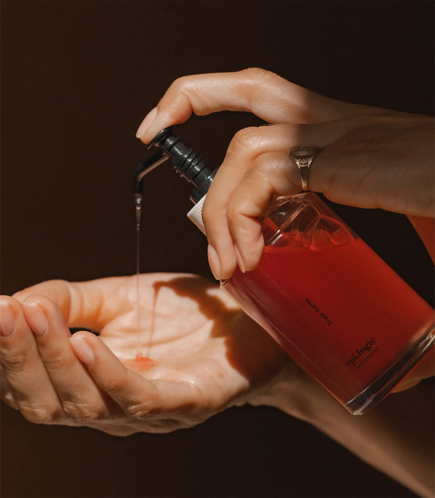 Hand pouring red liquid from a bottle into another hand against a dark background