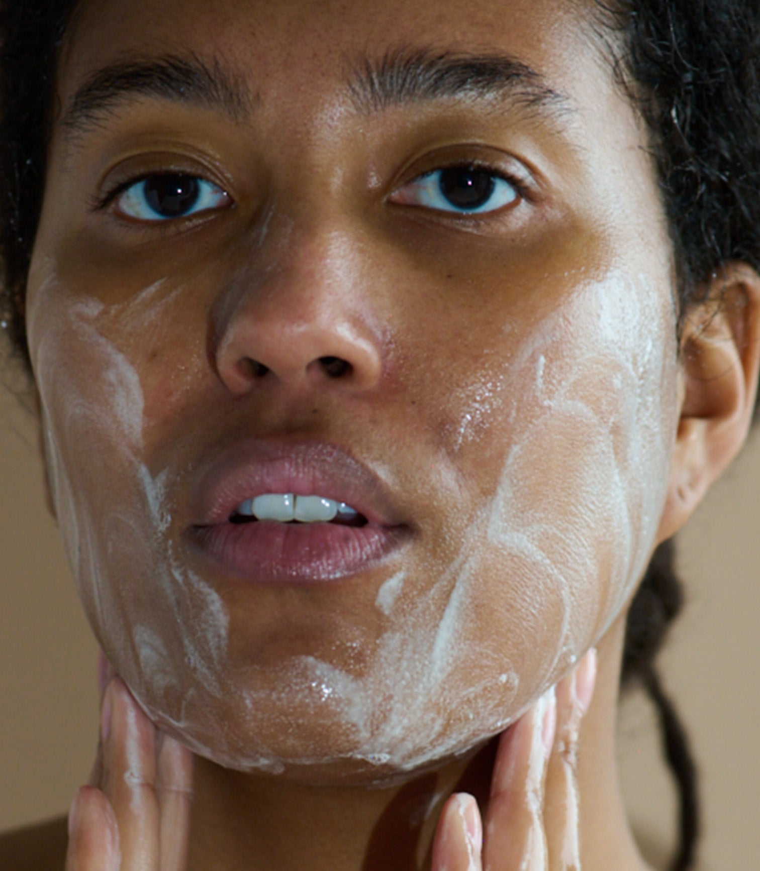 Person applying a facial mask with a neutral background